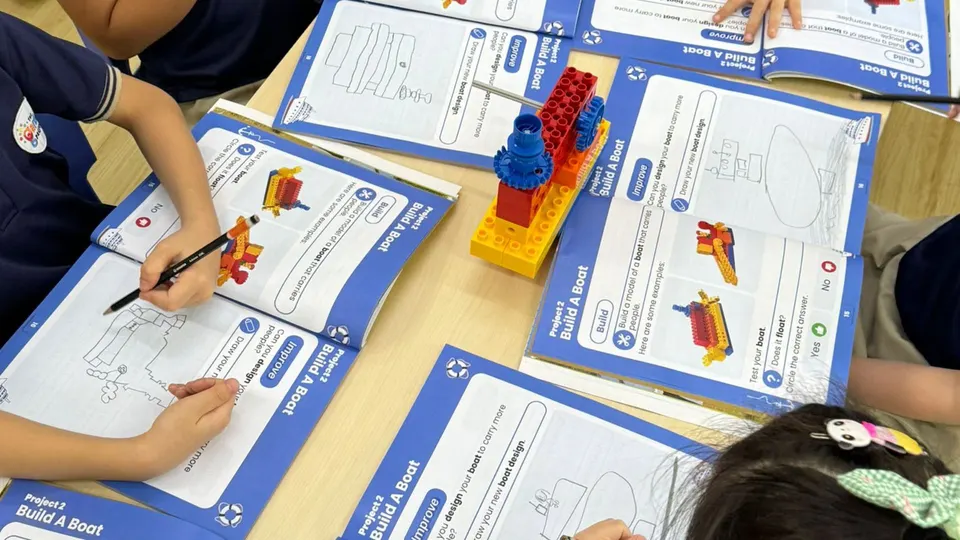 Workbooks open on a desk with a brick build and pencils, no faces